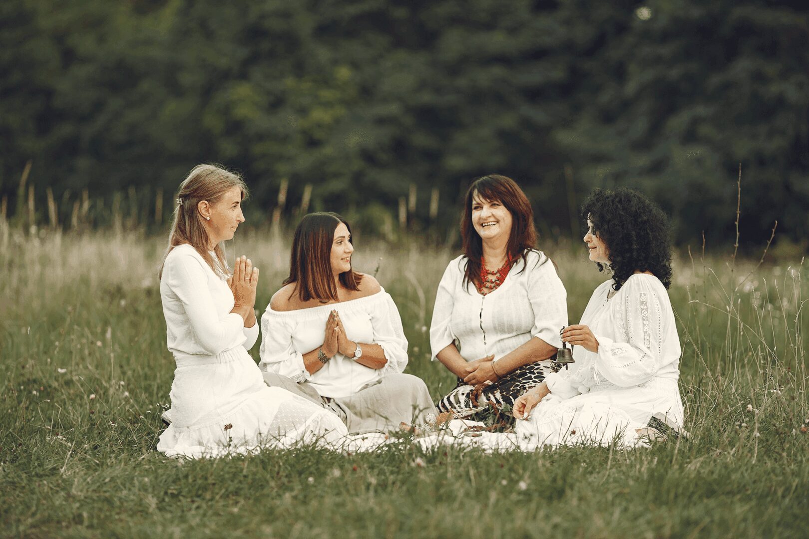 Four women in white dresses sitting in meadow