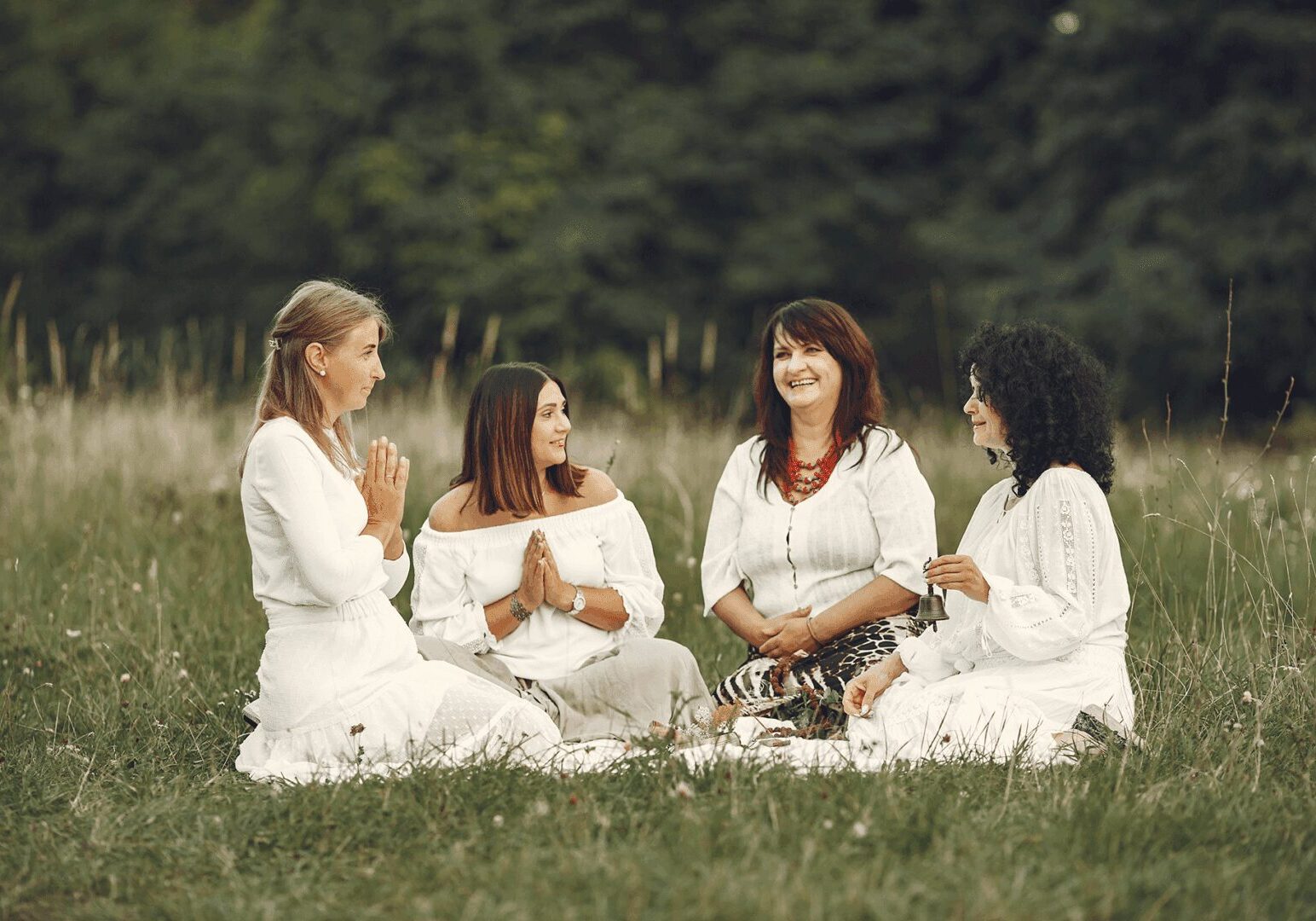 Four women in white dresses sitting in meadow